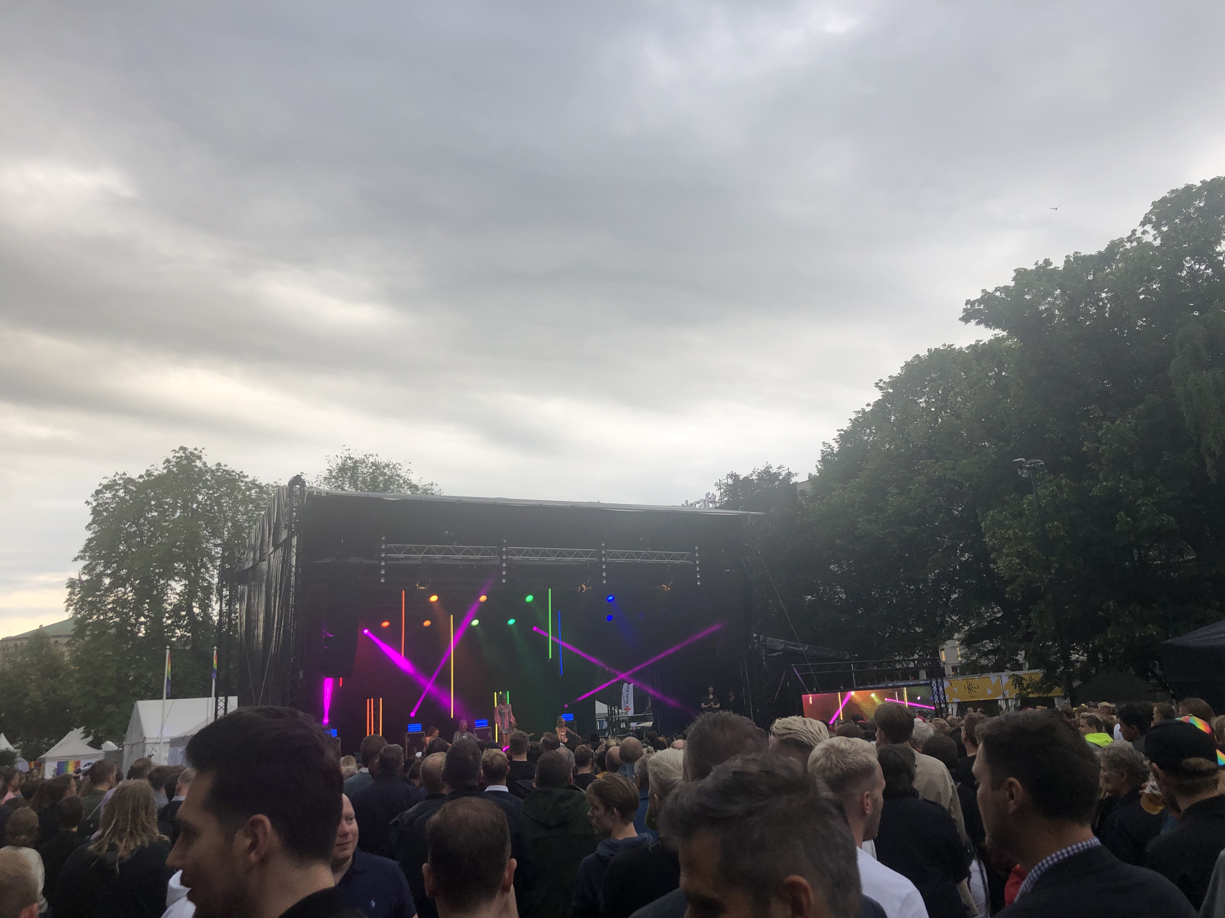 Oslo pride festival; large stage with flashing lights of all colors. Many people around. Gray skies.