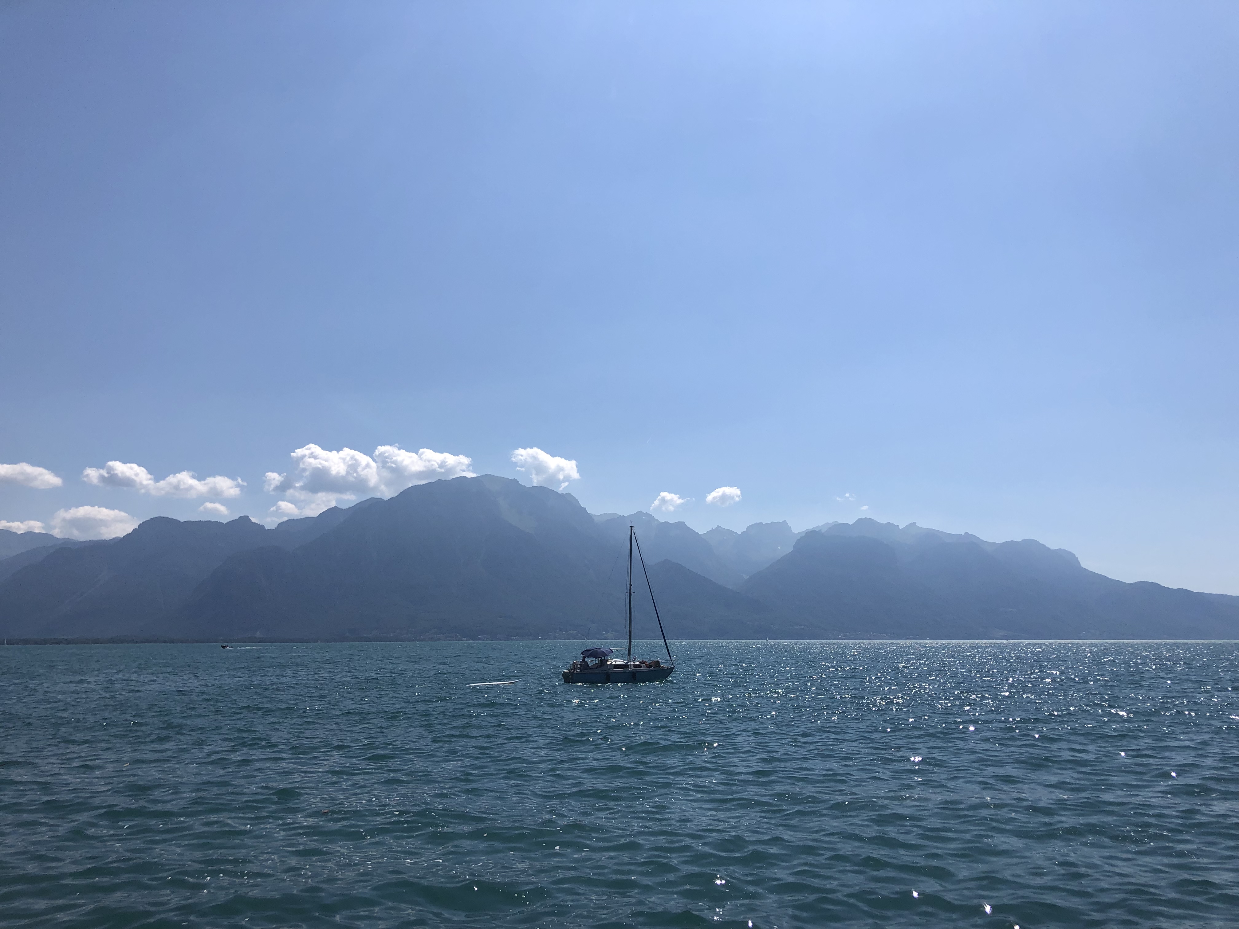 Lake Geneva with mountains in the background and a floating sailboat